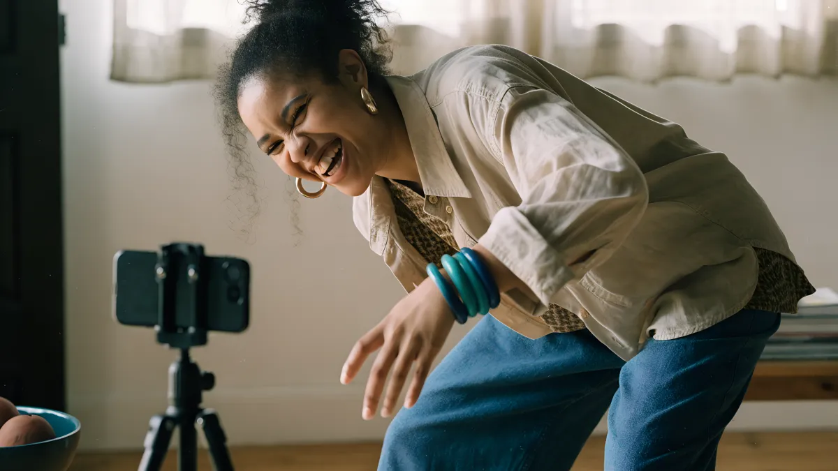 A young South African woman dancing in front of her phone on a tripod, filming herself