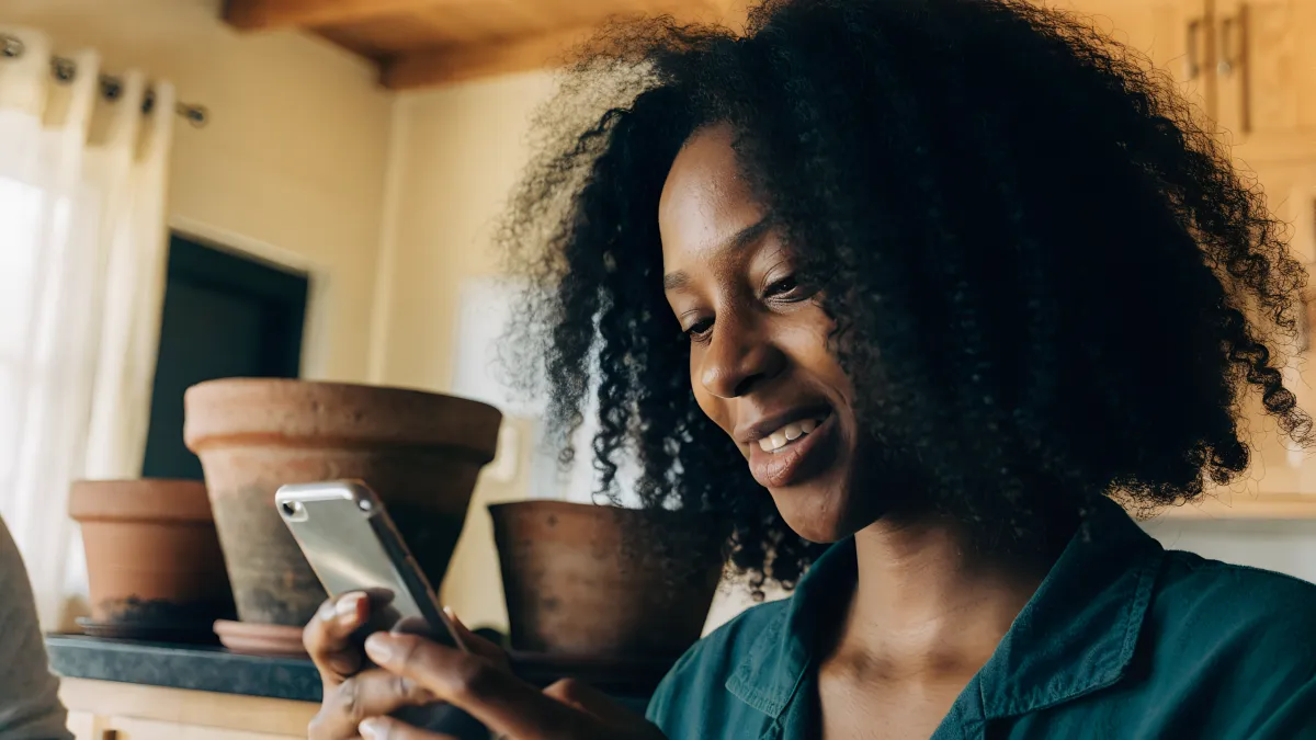 A South African woman smiling at her phone in a bright kitchen